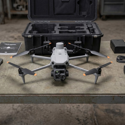 A gray DJI drone with four propellers and orange accent tips is displayed on a workbench in front of its open black carrying case, with accessories and a manual nearby.
