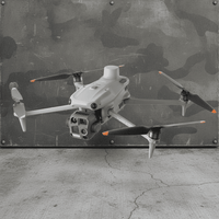 A light gray quadcopter drone with black and orange-tipped propellers, hovering in front of a distressed camouflage metal wall and concrete floor.