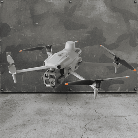 A light gray quadcopter drone with black and orange-tipped propellers, hovering in front of a distressed camouflage metal wall and concrete floor.